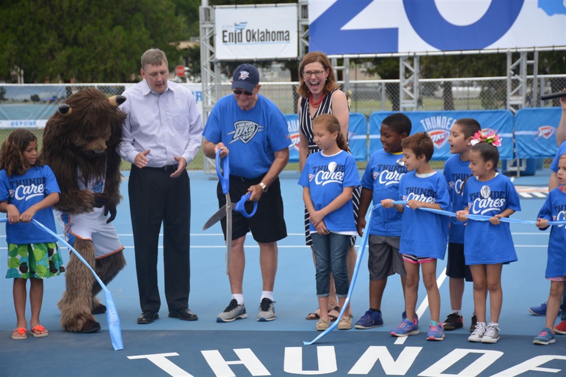 a group of people standing together cutting ribbon for a renovated outdoor basketball court