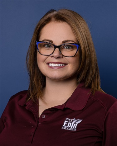 Photo of a woman wearing glasses and a burgundy shirt in front of a blue background
