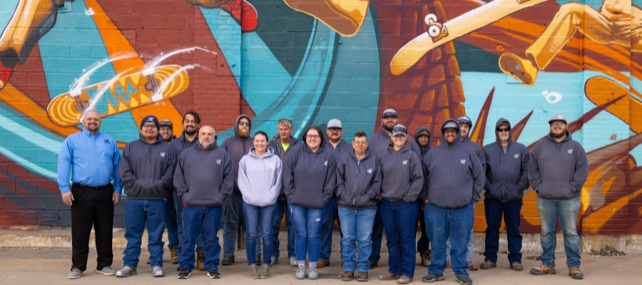 People standing in City of Enid t-shirts, in front of a painted wall smiling