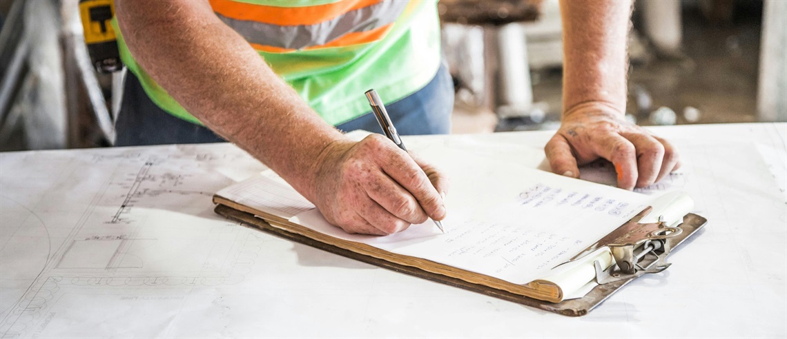 photo of man in a construction vest writing on a clipboard